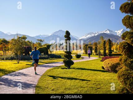 Young couple training in topiary park. Man is jogging and woman doing Nordic walking with poles. Healthy life concept. Stock Photo