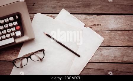 Typewriter, pensil, glasses and paper on wooden background. Creative writing and journalism concept Retro filtered image