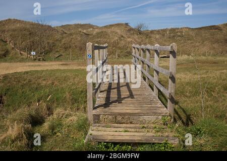 Wooden footbridge taking Wales Coast path over a tributary of the Ogmore river in Merthry Mawr nature reserve Stock Photo