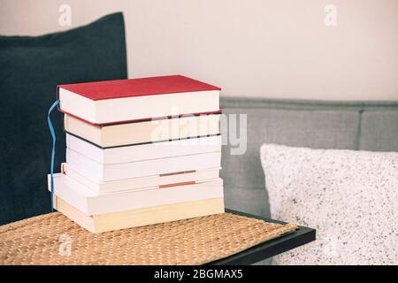 Book stack on the table with cozy sofa, cushions and pillows. Reading books, study at home, learning. Stock Photo