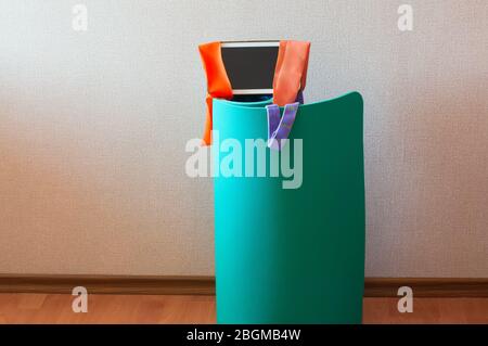 Fitness at home, stay home sport, online workout concept. Green mat and resistance bands with notepad in room interior. Stock Photo