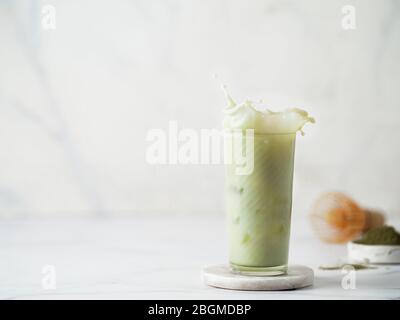 Homemade iced matcha latte with splashes on white marble background. Copy space for text or design