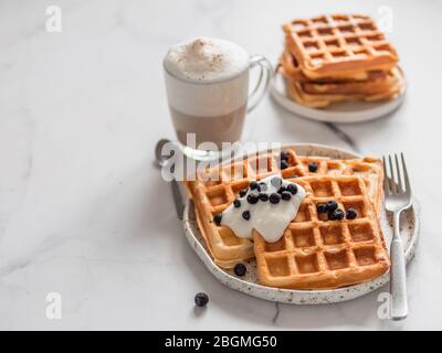 Delicious homemade baked belgian waffles with greek yogurt, blueberries and cappuccino on white marble background. Perfect breakfast with copy space for text or design Stock Photo