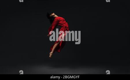 Contemporary dancer dancing on black studio background. Female dancer in red silk dress dancing barefoot in studio. Stock Photo