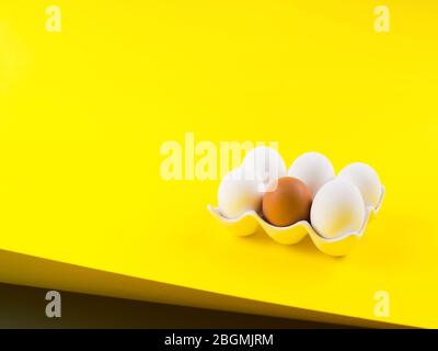 White and one brown egg on yellow bold color Stock Photo