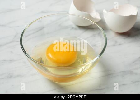 Fresh raw egg in a bowl close up with white shells in the background Stock Photo