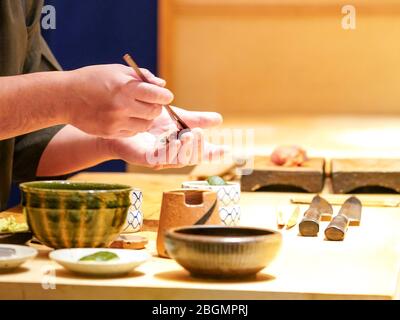 The chef is brushing shoyu sauce onto the raw fish. Enjoy Omakase experience at Japanese Sushi Restaurant. Stock Photo