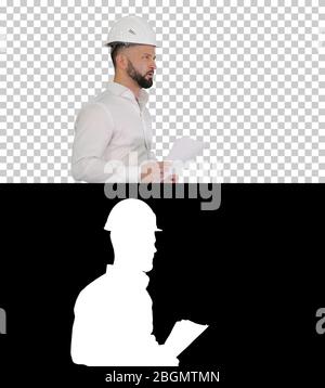 Male engineer walking in a hard hat looking at documents, Alpha Stock Photo