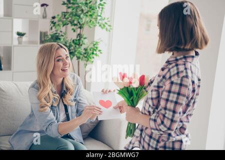Adorable two people 8-march celebration concept, Positive mommy sit cozy couch get receive present bloom blossom bunch tulips postcard from her Stock Photo
