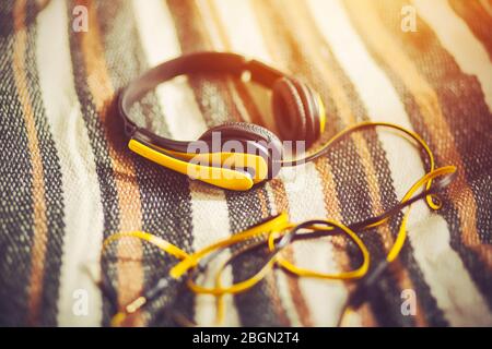 Bright yellow headphones with a microphone lie on a soft woolen striped blanket, illuminated by warm sunlight. Time to listen to music. Stock Photo