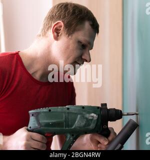 repair and decoration. man drills a hole in the wall Stock Photo