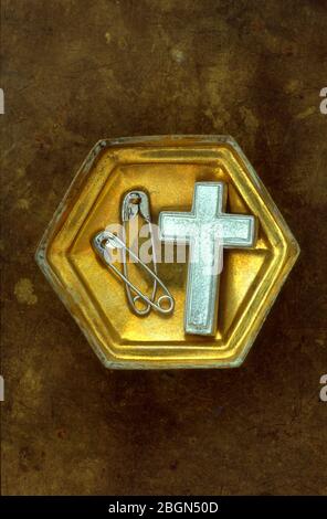 Small hexagonal brass box containing vintage silver crucifix and two used silver safety pins Stock Photo