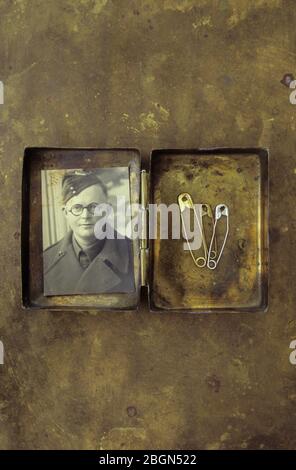 Vintage brass box containing three used safety pins and silver crucifix with hand coloured photo of 1950s girl Stock Photo