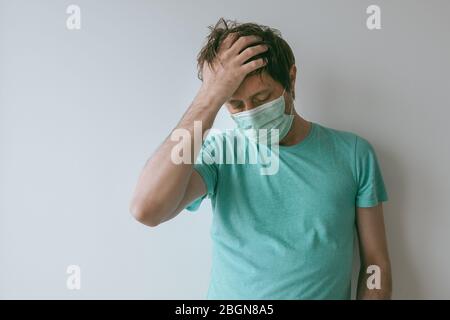 Man with mask having migraine headache as Covid-19 symptoms, portrait of male person with virus infection during pandemics Stock Photo