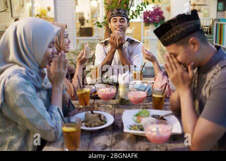 muslim family praying before eating their food. breaking the fast or iftar dinner Stock Photo
