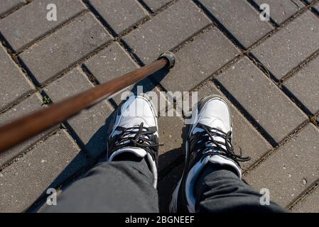 Legs of a young guy in sneakers, with a cane for walking. For any purpose. Stock Photo