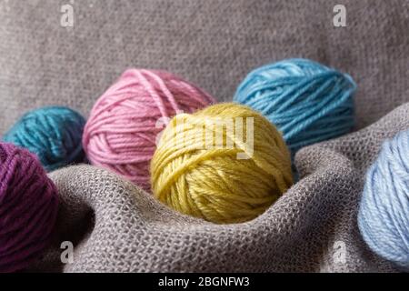 Knitting hobby. Multi-colored tubes of wool on gray plaid. Cozy hugge hobby. Close up. Stock Photo