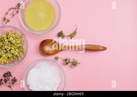 Close up of Ingredients of ayurvedic treatment or face pack. Yellow clay, turmeric powder and dried chamomile, sea coarse salt in glass cups on a pink pastel colour background. Flat lay blog style. Stock Photo