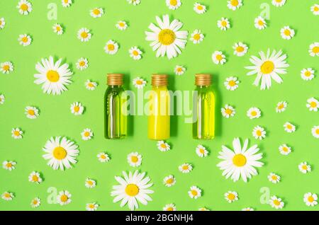 Flat lay of small mockup bottles with spa cosmetic products on green background with fresh camomile blossoms. Women beauty and beauty salon cosmetics Stock Photo