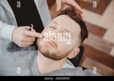 Barber hairdresser applies foam and beard shaving lotions to male client. Cream and oil skin care concept Stock Photo