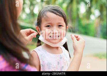 Mother is wearing medical mask for little girl protect herself from Coronavirus when child leave house to public area mom is wearing mask on nose for Stock Photo