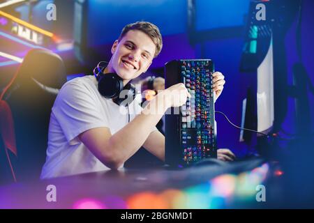 Professional young man player in online video game cybersportsman advertises headphones, keyboard and mouse for computer, blurred background Stock Photo