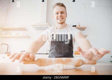 Chef happy man Italian rolls dough on wooden table against of window, light kitchen background Stock Photo