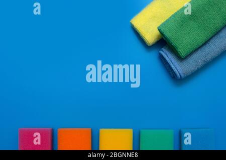 Three colorful, dry microfiber cloths and rainbow colored sponges for cleaning various surfaces in the kitchen, bathroom and other rooms, on a blue ba Stock Photo