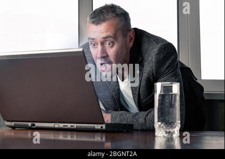 Shocked businessman looking at laptop screen with surprised expression.. Surprised businessman looks wide-eyed at laptop screen. Work at home. Office Stock Photo