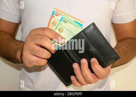 Kazakhstan national currency. KZ money banknotes. Man in white t shirt put tenge banknotes into black wallet, man holds in hands wallet with kz money Stock Photo