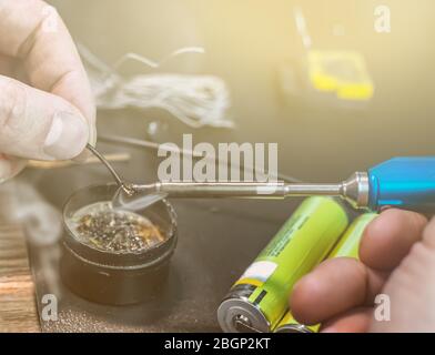 technical master soldering parts with a soldering iron. resin, the smoke, the battery, wires. technical support, repair Stock Photo