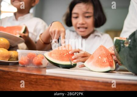 kid slicing watermelon using knife on chopping board Stock Photo