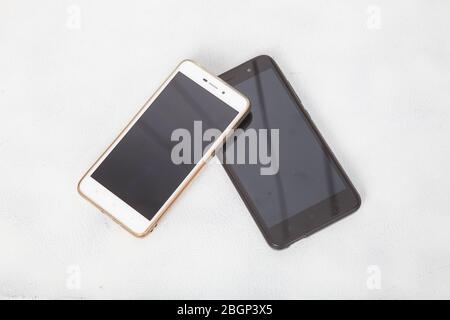 two modern smartphones are lying on the white surface of the table Stock Photo