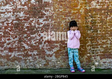Asian female child wearing pink jacket cute pose with old brick wall background Stock Photo