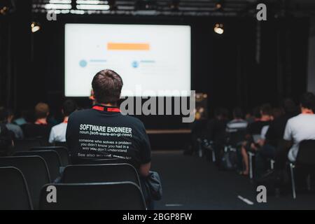 Software engineer in black t-shirt sitting in conference hall during programming worshop in full hall with audience learning programming Stock Photo