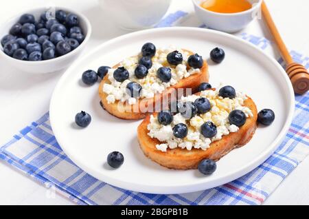 Sandwiches with curd cheese, blueberries and honey on white plate, close up view Stock Photo