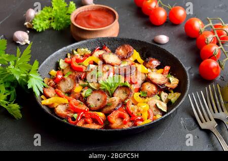 Slices of fried sausages with vegetables and spices in frying pan Stock Photo