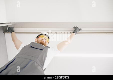 Male builder carpenter installs curtain on ceiling, bottom view Stock Photo