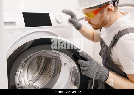 Plumber repairing washing machine, working man fixing problem Stock Photo