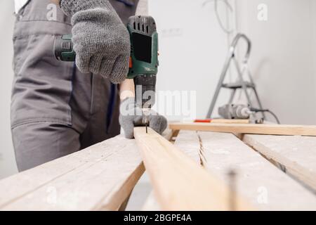 Worker man carpenter screws metal into wooden board with electric screwdriver Stock Photo