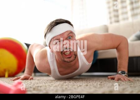 Funny grimacing man making push-ups home Stock Photo