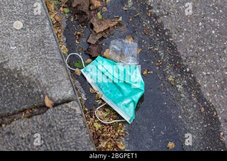 Used, green surgical mask on a sidewalk / road. Lost or thrown away. Covered with dirt. Protective mask, becoming more & more common due to Covid-19. Stock Photo