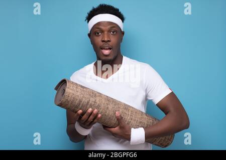 Fitness Concept. Happy black man yoga mat, smiling at camera over blue wall Stock Photo