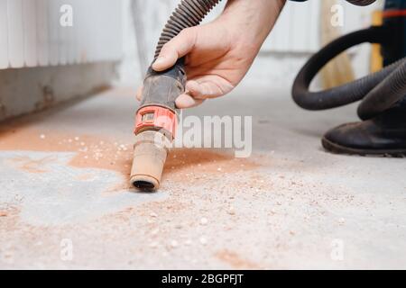 Worker vacuuming debris and dust from floor after drilling concrete wall Stock Photo