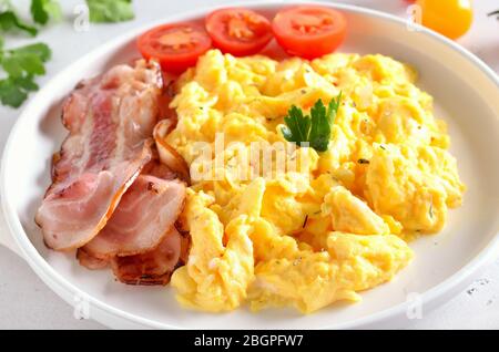 Scrambled eggs, fried bacon and tomatoes on white plate, close up view Stock Photo