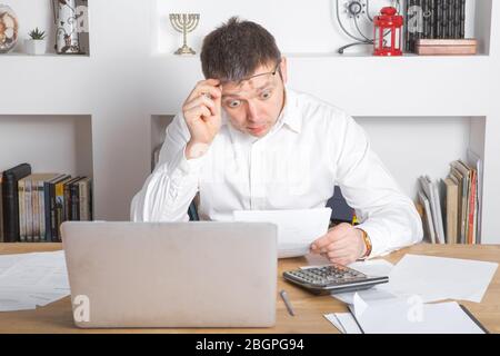 Businessman receiving negative news, touching his glasses, being mad, upset and surprised in front of laptop. Stock Photo