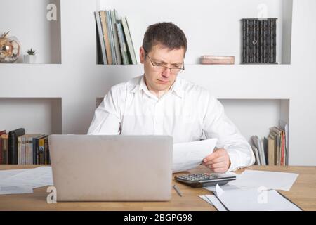 Businessman receiving negative news, touching his glasses, being mad, upset and surprised in front of laptop. Stock Photo