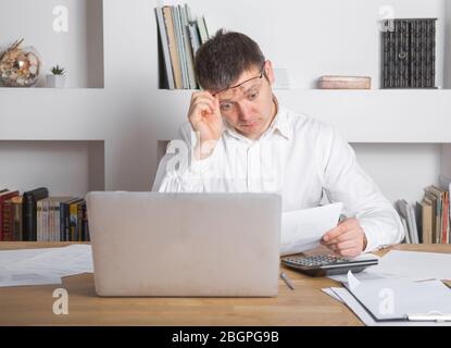Businessman receiving negative news, touching his glasses, being mad, upset and surprised in front of laptop. Stock Photo