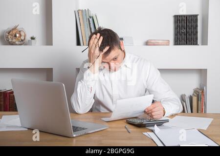 Businessman receiving negative news, touching his glasses, being mad, upset and surprised in front of laptop. Stock Photo