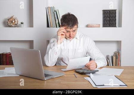 Businessman receiving negative news, touching his glasses, being mad, upset and surprised in front of laptop. Stock Photo